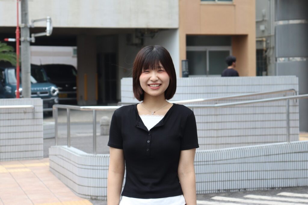 黒いトップス姿で屋外に立つ鶴結びの新メンバー